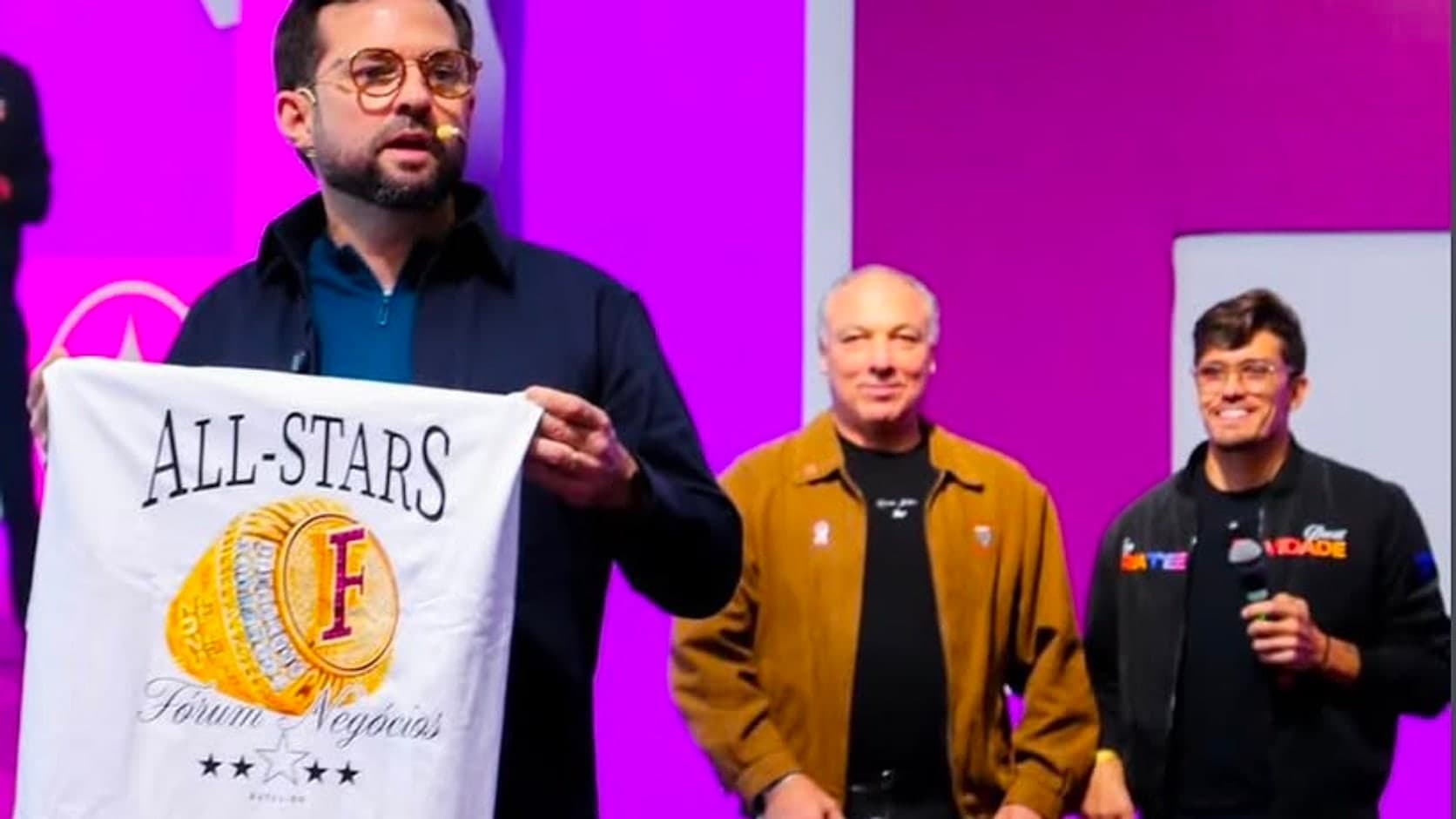Camiseta All-Stars do Fórum Negócios erguida no palco do evento diante da plateia
